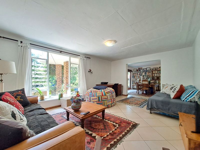 Spacious living room with tiled flooring, large windows providing natural light, and an open-plan layout connecting to an adjacent dining area.