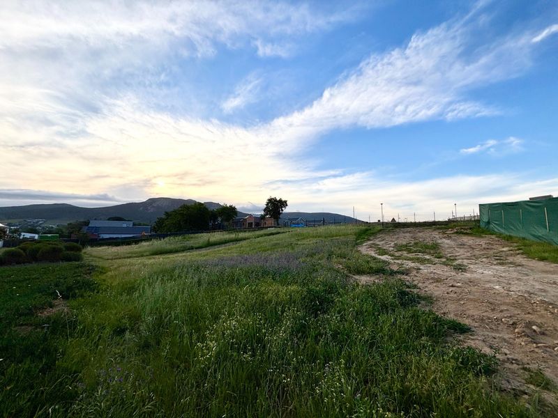 A scenic view of the vacant residential land featuring natural grass, an unpaved access track, and distant mountain vistas under a clear sky.