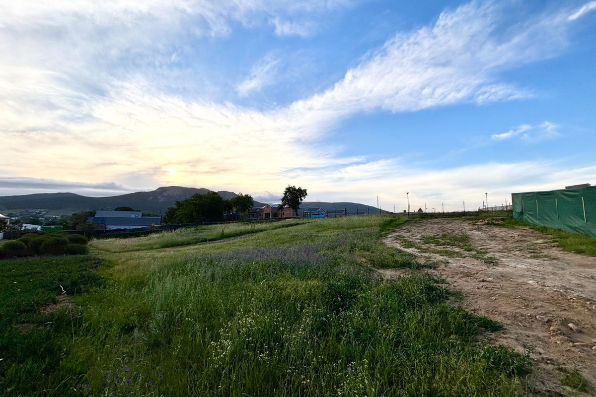 A scenic view of the vacant residential land featuring natural grass, an unpaved access track, and distant mountain vistas under a clear sky.
