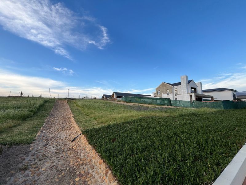 A view of a residential plot featuring a cobblestone pathway leading towards a house currently under construction.