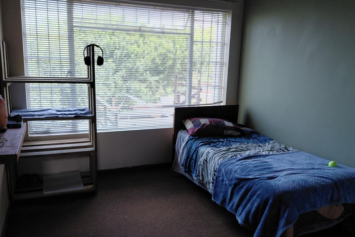 A standard bedroom featuring carpet flooring and large windows fitted with venetian blinds, offering natural light and a view of the outdoors.
