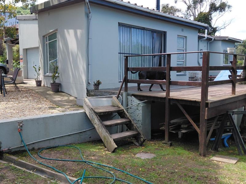 Rear exterior view featuring a raised timber deck with balustrade, sliding door access, and a retaining wall leading to the garden area.