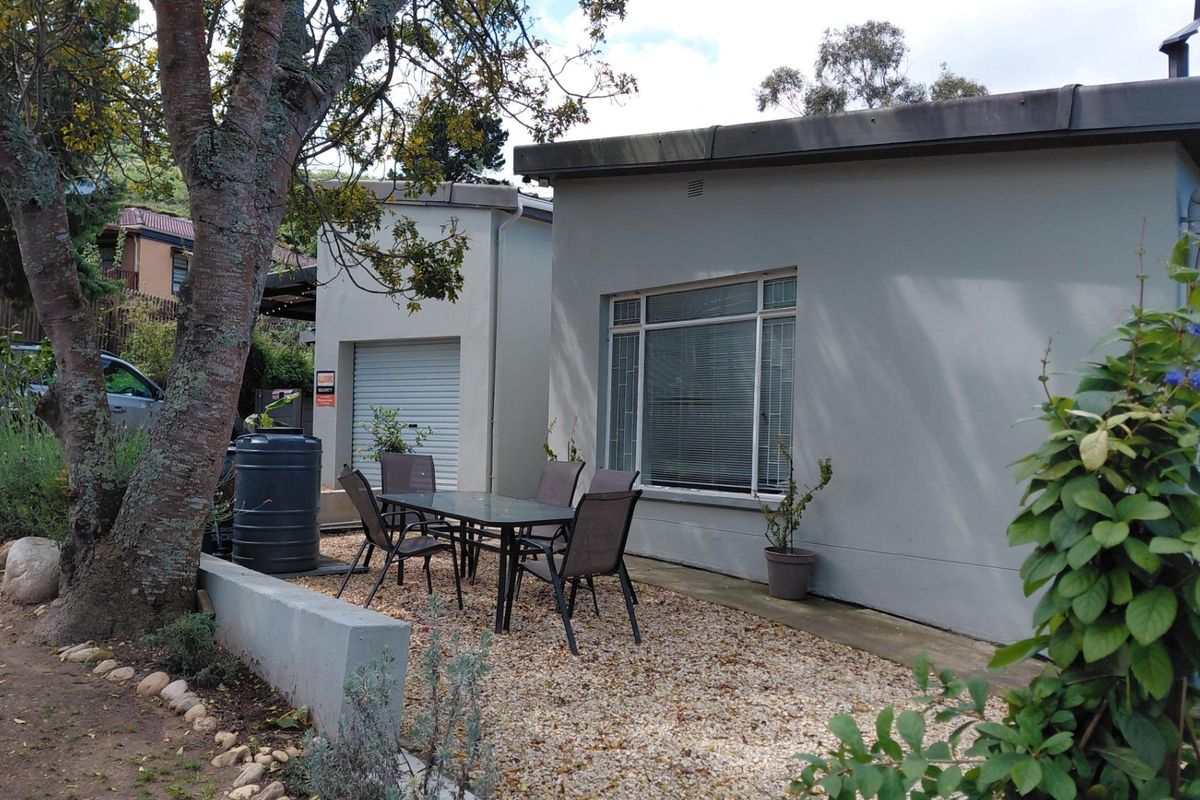 Rear exterior view showing a gravel patio area, a single garage with a roller shutter door, and a low retaining wall.