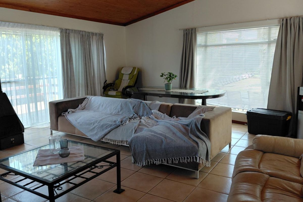 Spacious living room featuring tiled flooring, a wood-paneled ceiling, and a freestanding fireplace, with large windows and sliding doors providing natural light.
