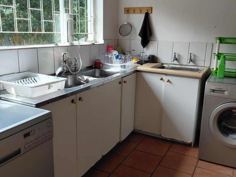 Functional laundry area featuring a stainless steel double sink, tiled backsplash, and built-in cabinetry with terracotta floor tiles.