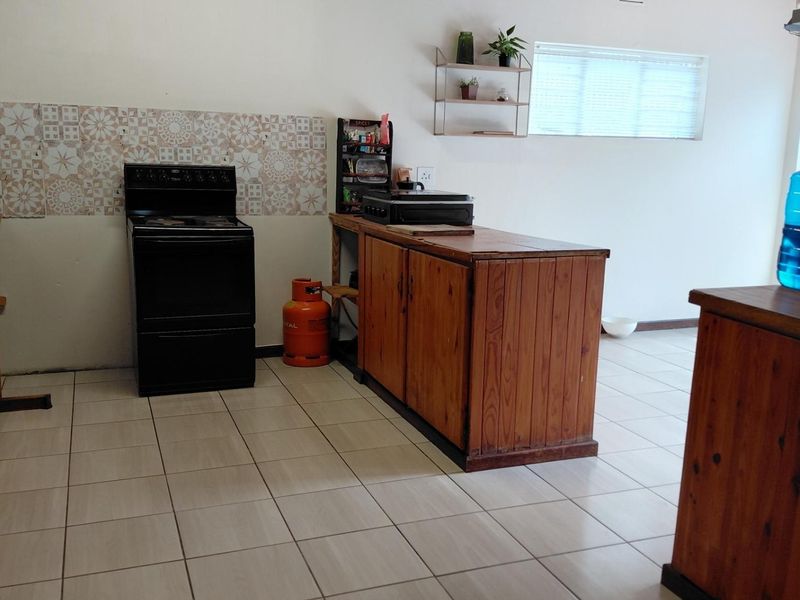 A functional kitchen featuring tiled flooring, a patterned tile backsplash, and wooden cabinetry with a freestanding stove.
