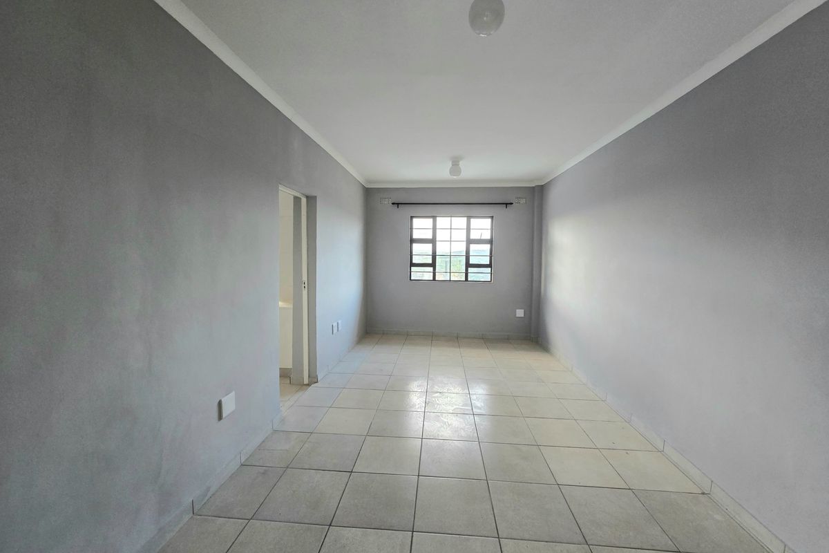 An empty, neutrally painted living area featuring tiled flooring, coved ceilings, and a grid-pattern window, offering a blank canvas for personalization.