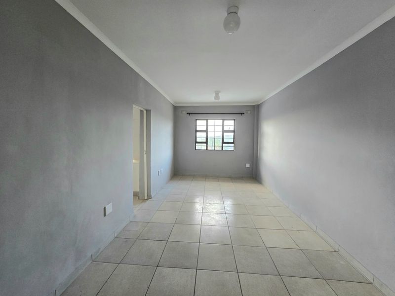An empty, neutrally painted living area featuring tiled flooring, coved ceilings, and a grid-pattern window, offering a blank canvas for personalization.