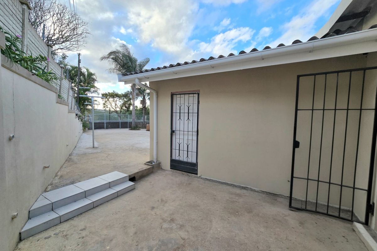 Rear exterior area featuring concrete paving, a security gate, and tiled steps leading to a retaining wall.