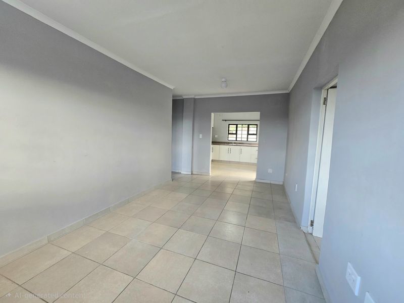 An empty open-plan living area with neutral tiled flooring and walls, leading into a functional kitchen space with built-in cabinetry.