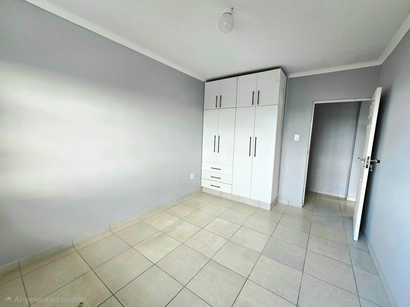 A clean, empty bedroom featuring neutral grey walls, light-colored floor tiles, and white built-in cupboards with modern black handles.