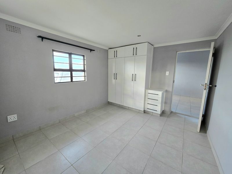 A clean, neutral bedroom featuring tiled flooring, built-in white cabinetry, and security bars on the window, offering a bright and well-maintained living space.