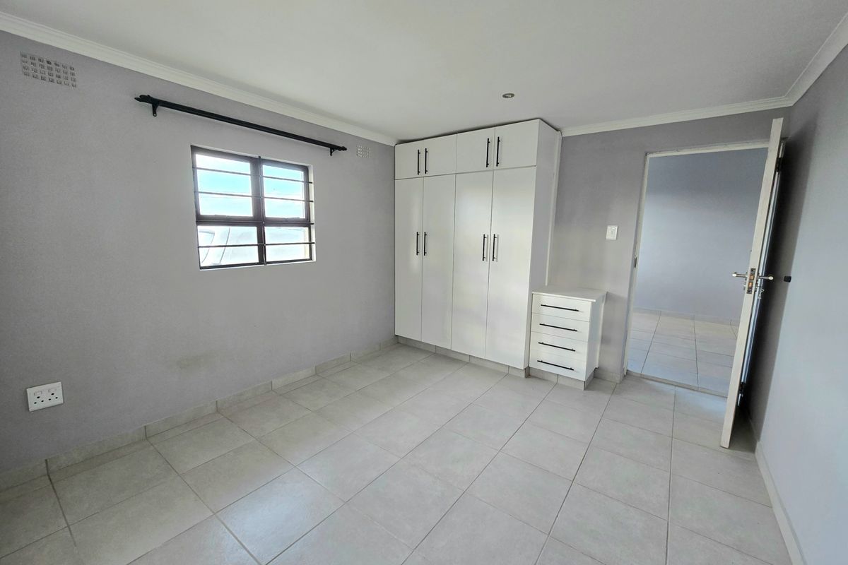 A clean, neutral bedroom featuring tiled flooring, built-in white cabinetry, and security bars on the window, offering a bright and well-maintained living space.