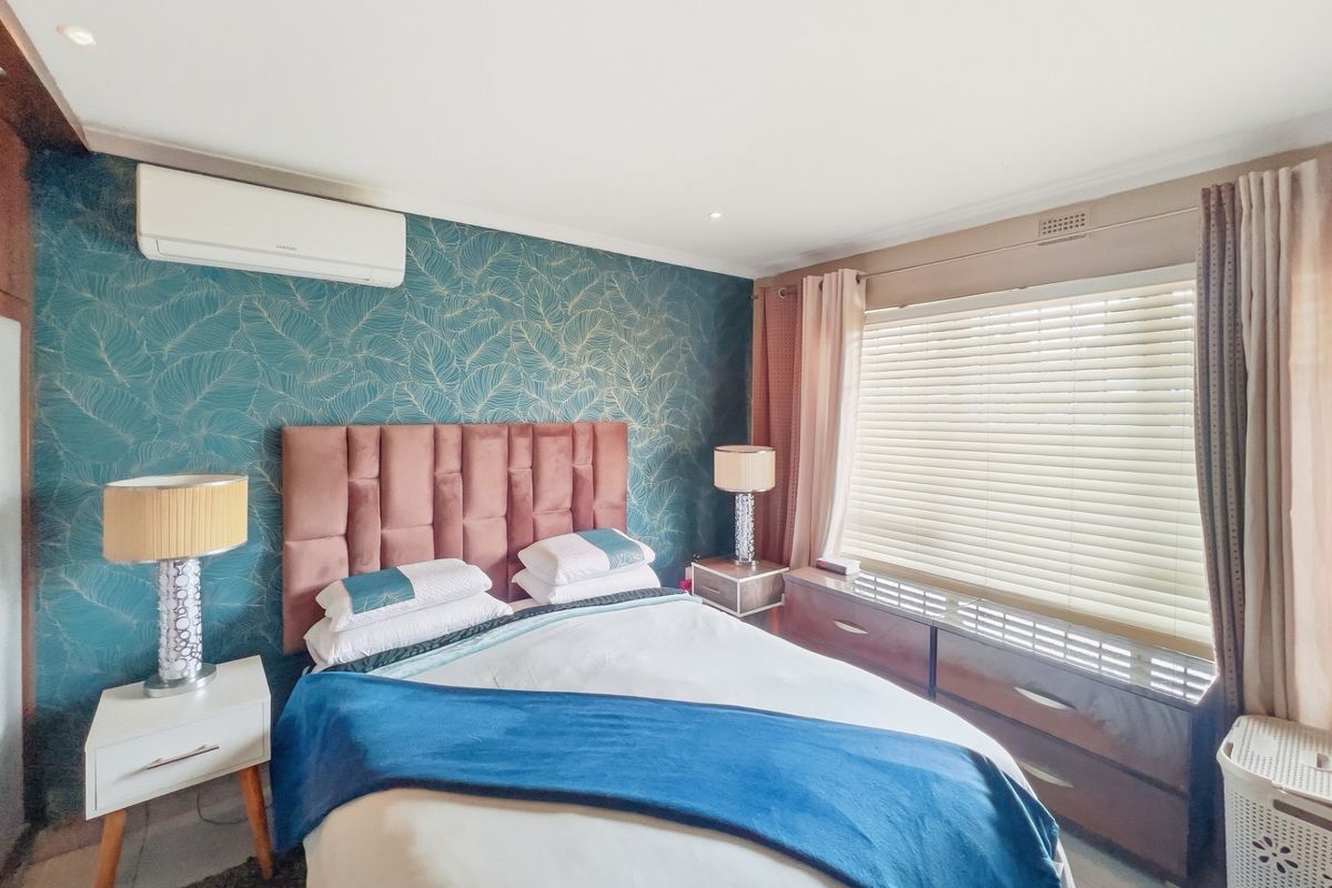 A well-maintained bedroom featuring a feature wall with patterned wallpaper, split-system air conditioning, and venetian blinds for light control.