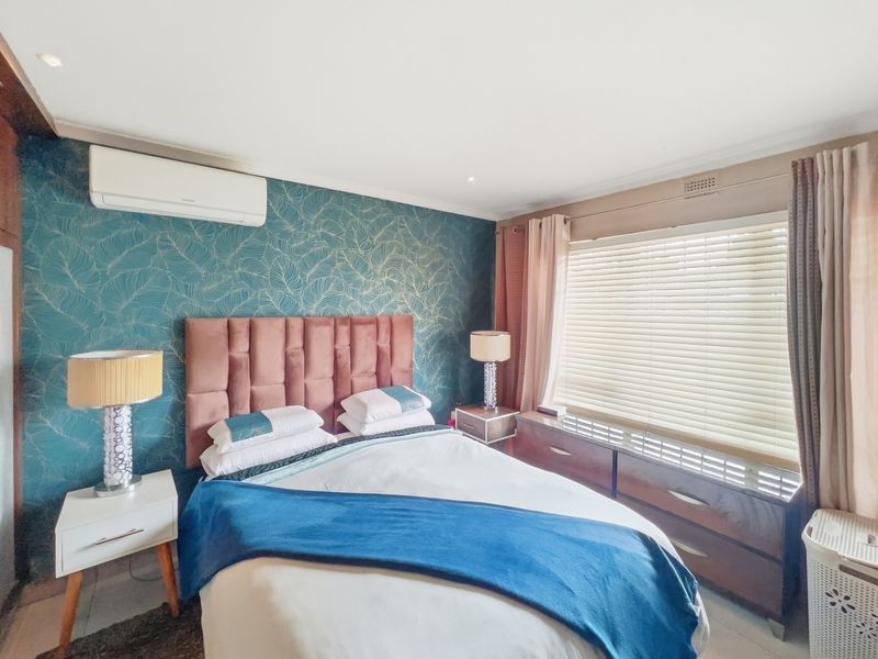 A well-maintained bedroom featuring a feature wall with patterned wallpaper, split-system air conditioning, and venetian blinds for light control.
