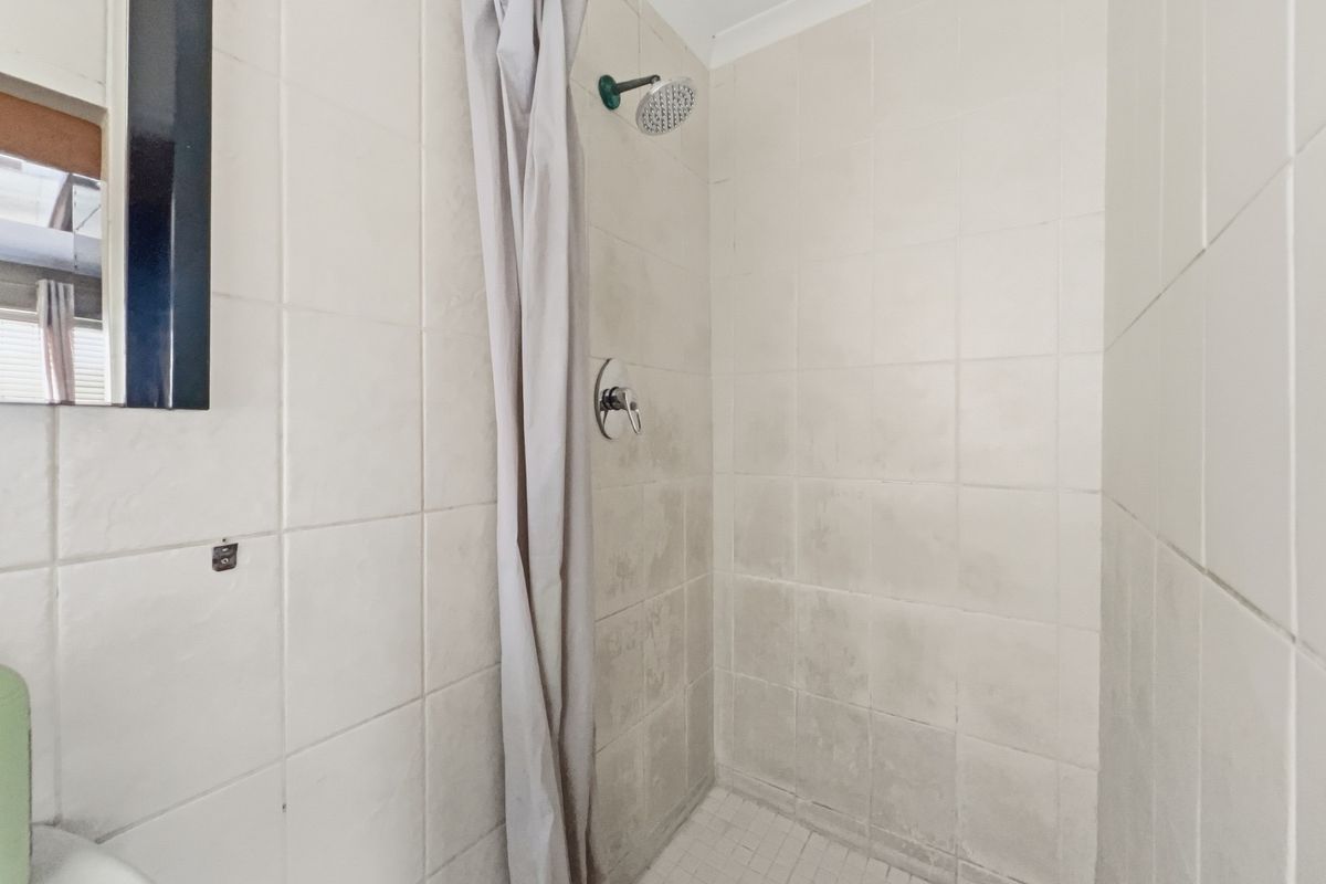 A functional bathroom shower area featuring tiled walls and floor, currently showing signs of wear and staining on the tile surfaces.