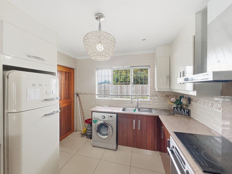 A functional kitchen featuring wood-finish lower cabinetry, white upper cabinets, tiled backsplash, and integrated appliances including a hob, oven, and extractor fan.