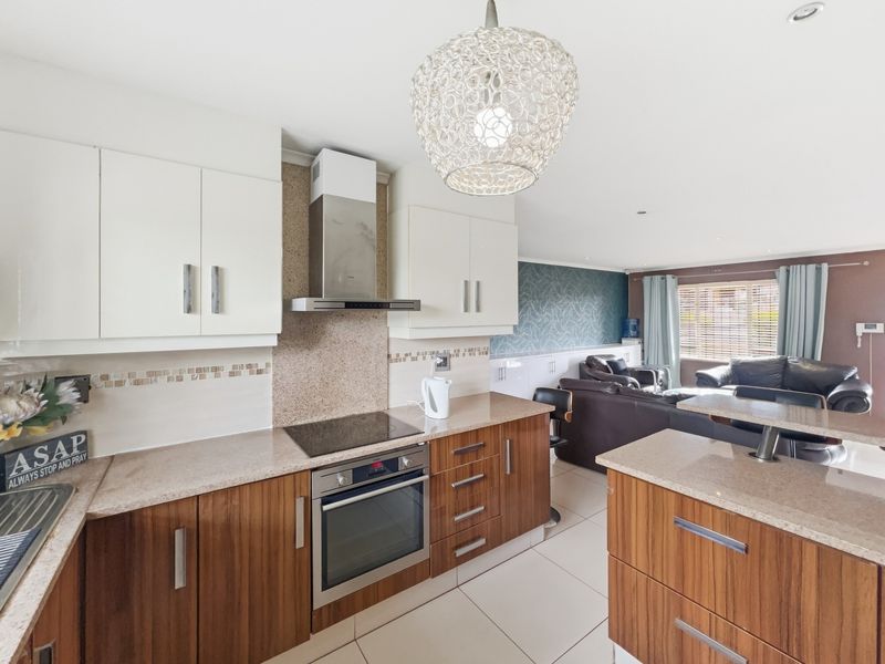 Modern open-plan kitchen featuring wood-grain and white cabinetry, stone countertops, integrated appliances, and seamless flow into the adjacent living area.