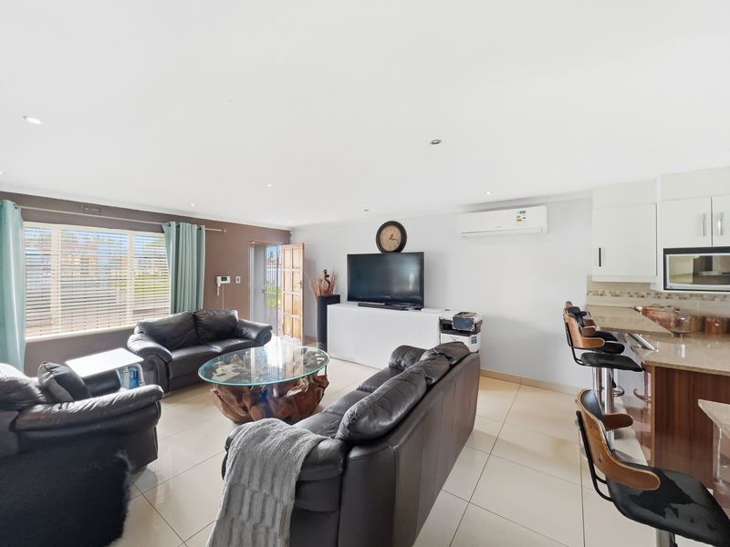 Spacious open-plan living area featuring tiled floors, recessed lighting, a split-system air conditioner, and a functional kitchen with granite countertops and a breakfast bar.