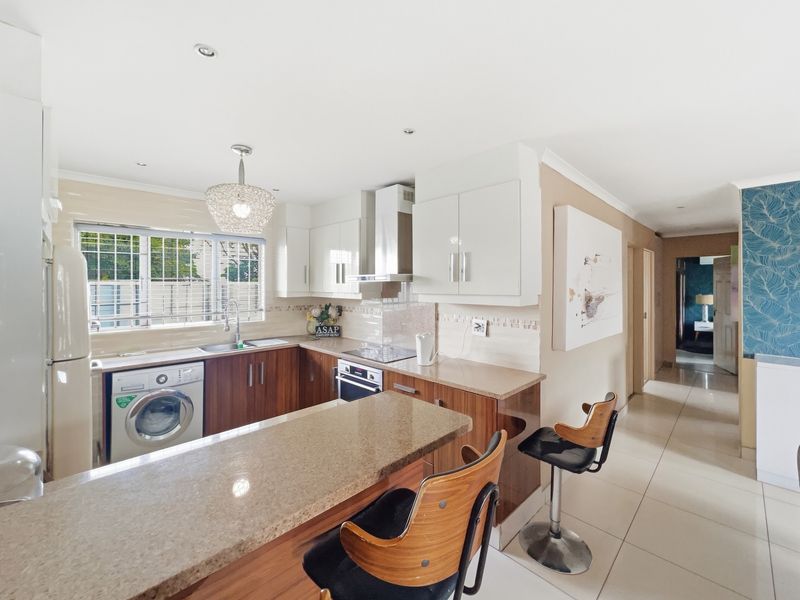 Modern kitchen featuring wood-finish cabinetry, granite countertops, integrated appliances, and a breakfast bar, seamlessly flowing into the home's hallway.