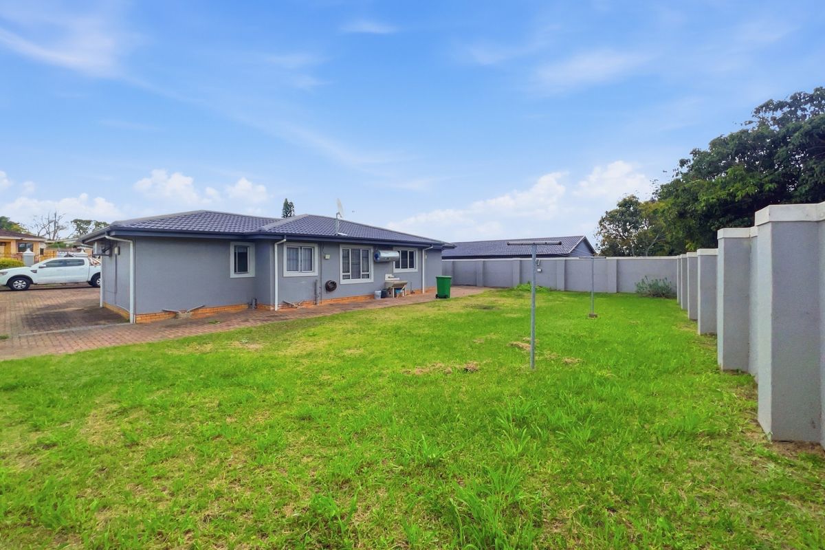 Rear view of the property featuring a spacious lawn, paved walkway, perimeter boundary wall, and external wash basin.