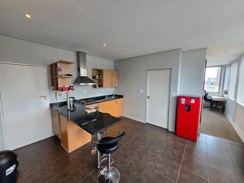 A functional kitchen featuring granite countertops, light wood cabinetry, a stainless steel extractor fan, and tiled flooring, with an open-plan layout.