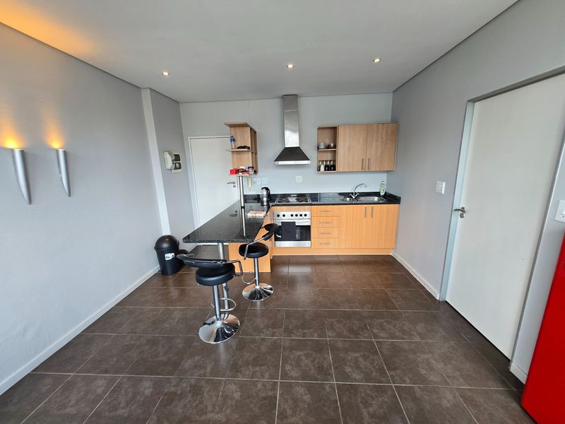 A functional kitchen featuring light wood cabinetry, granite countertops, a built-in oven with extractor fan, and tiled flooring with an integrated breakfast bar.
