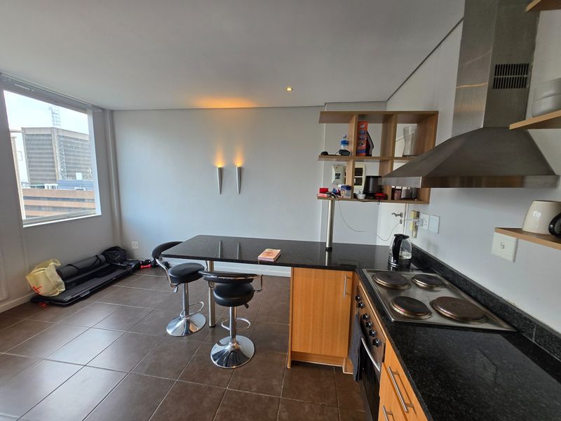 Open-plan kitchen featuring granite countertops, electric hob, built-in oven, and stainless steel extractor fan, complemented by tiled flooring and modern wall lighting.