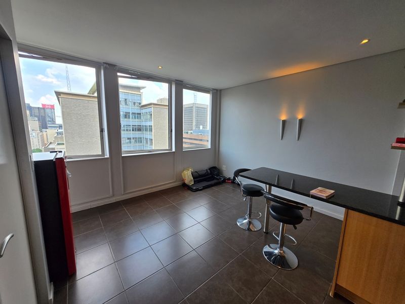Open plan living area featuring large windows with city views, tiled flooring, and a built-in breakfast bar with integrated lighting.