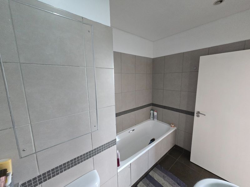 A functional bathroom featuring neutral wall tiles with a decorative mosaic border and a built-in bathtub.