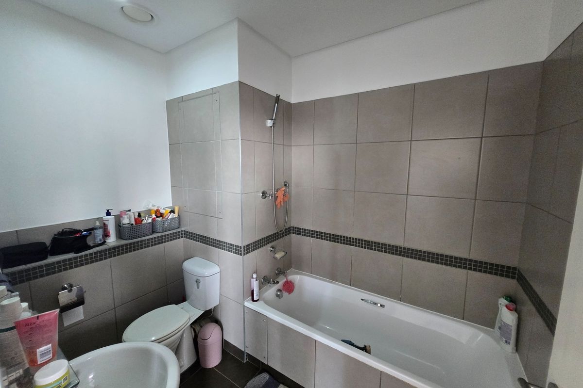 A functional bathroom featuring a built-in bathtub with shower attachment, a pedestal basin, and a toilet, finished with neutral wall and floor tiling.