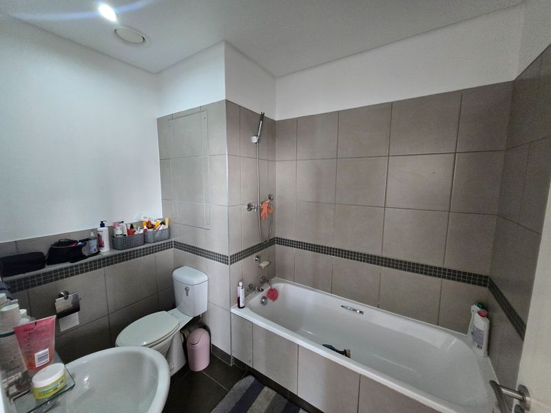 A functional bathroom featuring a built-in bathtub with shower attachment, a pedestal basin, and a toilet, finished with neutral wall and floor tiling.