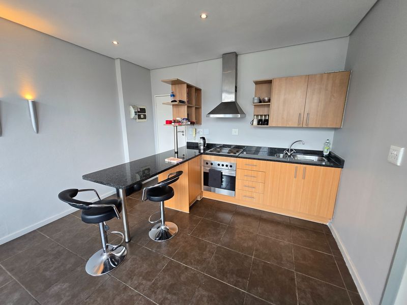 Modern kitchen featuring granite countertops, wooden cabinetry, stainless steel appliances, and a breakfast bar, complemented by tiled flooring and recessed lighting.