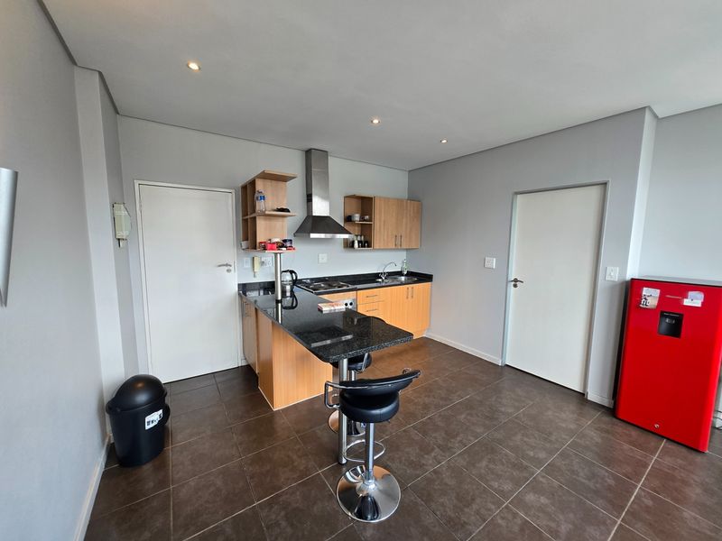 Compact kitchen featuring granite countertops, built-in wooden cabinetry, a stainless steel extractor fan, and tiled flooring with recessed lighting.