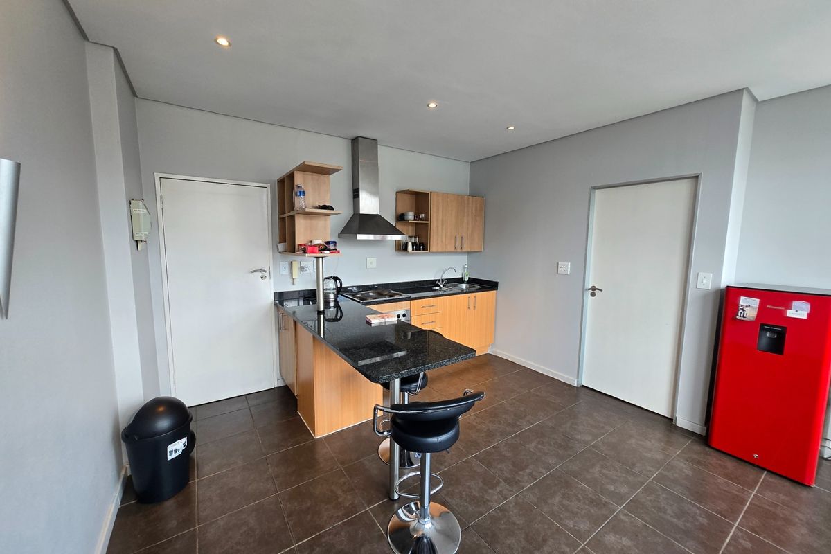 Compact kitchen featuring granite countertops, built-in wooden cabinetry, a stainless steel extractor fan, and tiled flooring with recessed lighting.