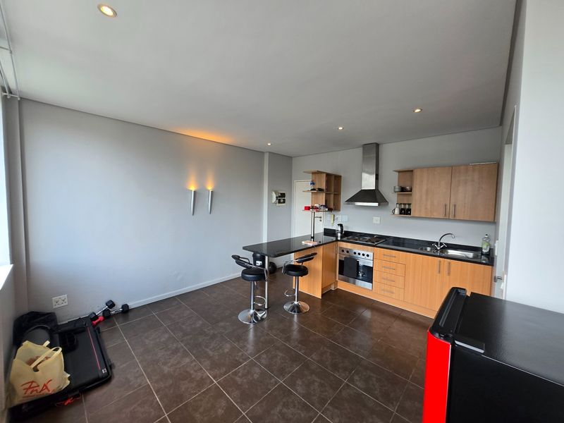 Open-plan kitchen featuring wooden cabinetry, granite countertops, integrated stainless steel appliances, and tiled flooring, seamlessly flowing into the living area.