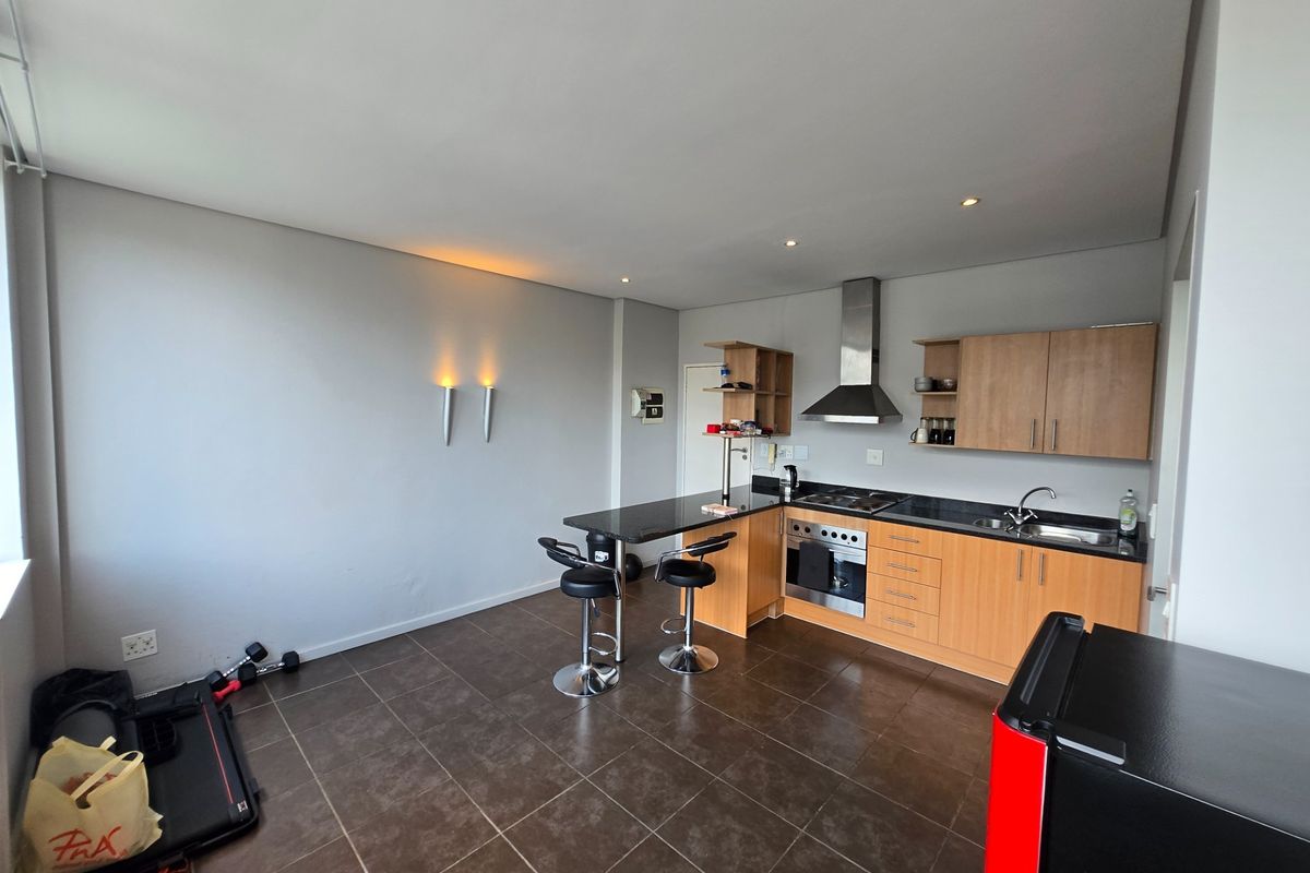 Open-plan kitchen featuring wooden cabinetry, granite countertops, integrated stainless steel appliances, and tiled flooring, seamlessly flowing into the living area.