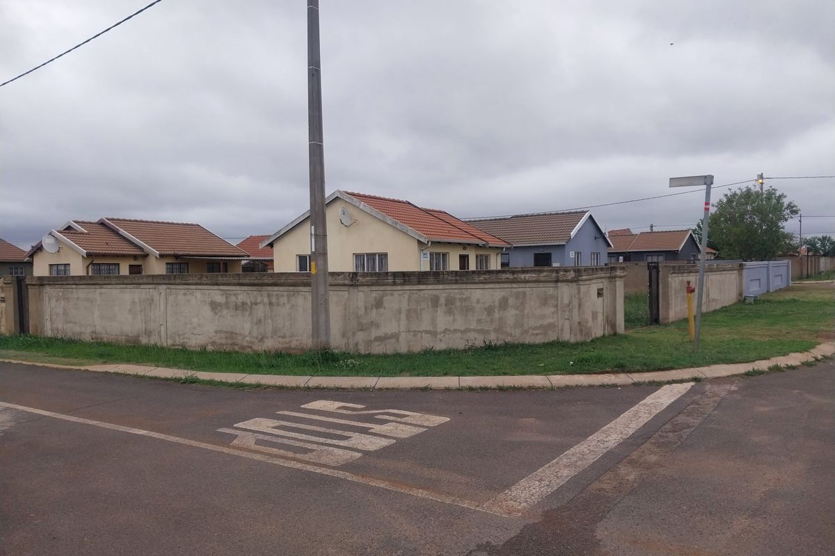 Street view of a residential property corner lot featuring a perimeter wall and tiled roof houses.