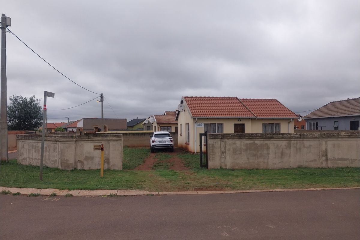 Front view of a single-story residential house featuring a tiled roof and a perimeter boundary wall with a gated driveway entrance.