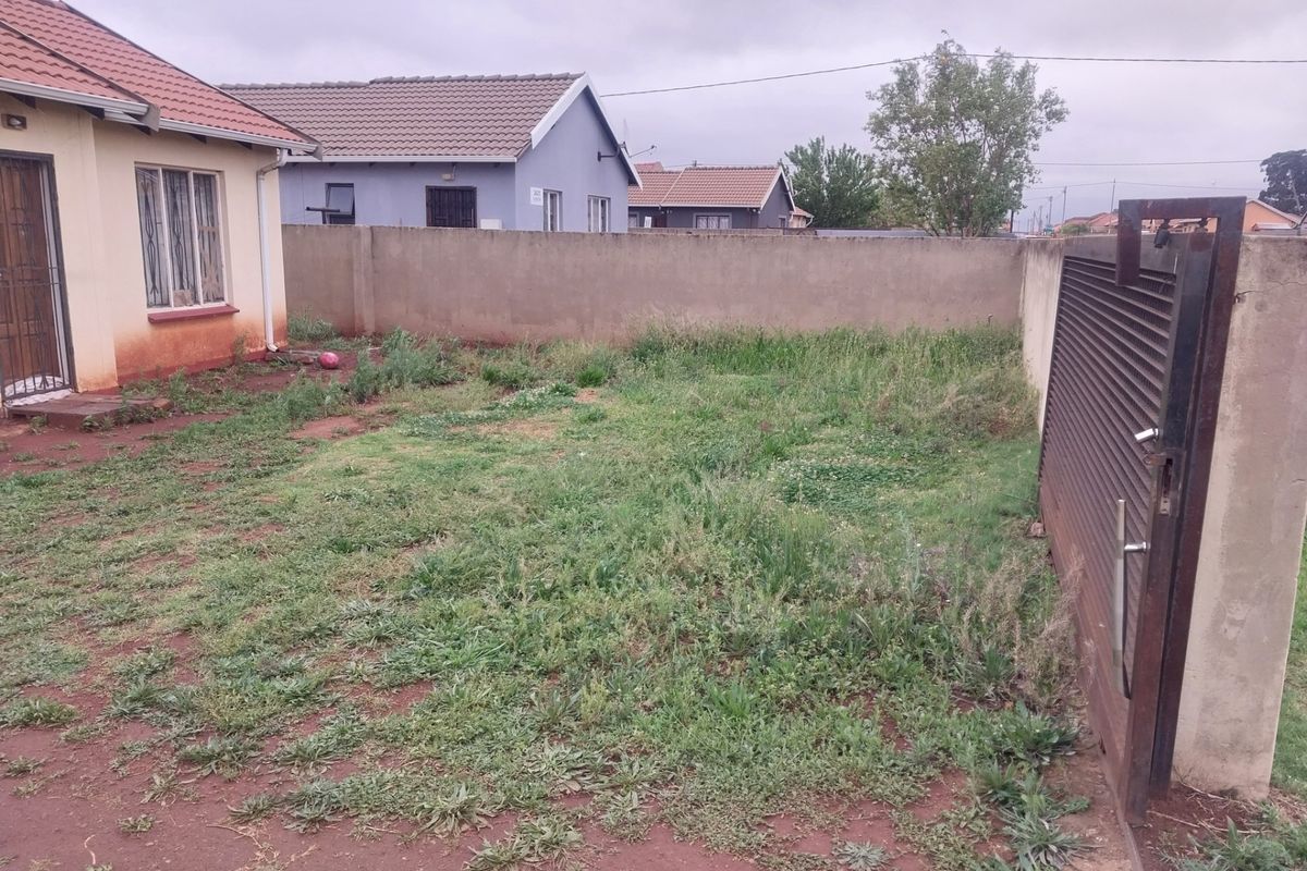 A rear garden area featuring a perimeter boundary wall, a sliding metal gate, and direct access to the main dwelling.