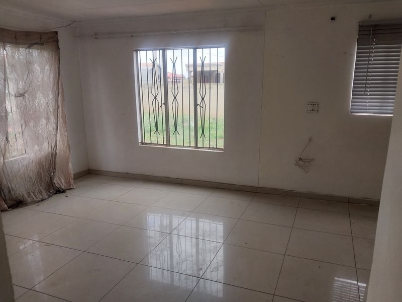An empty living room featuring tiled flooring, security bars on the windows, and venetian blinds, requiring minor cosmetic updates to wall finishes.