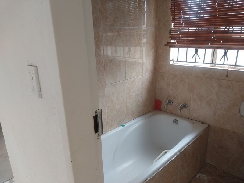 A functional bathroom featuring a built-in bathtub with wall-mounted taps, finished with neutral ceramic wall tiles and fitted with security bars.