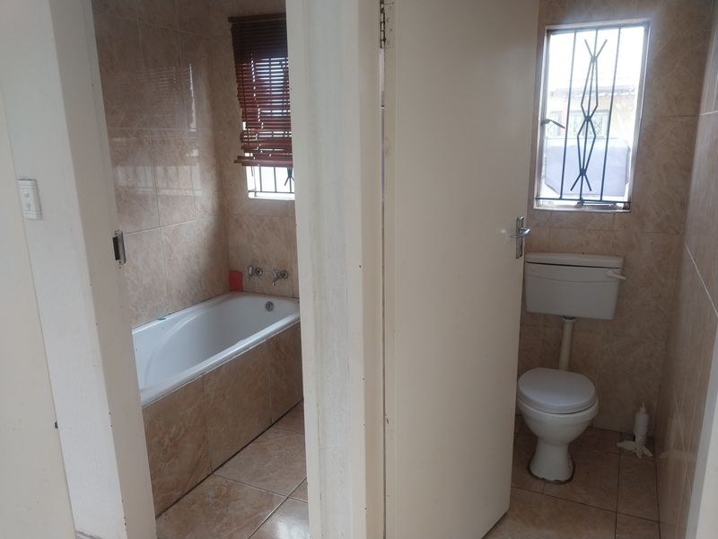 A functional bathroom featuring a built-in bathtub and separate toilet area, finished with neutral ceramic wall and floor tiles.