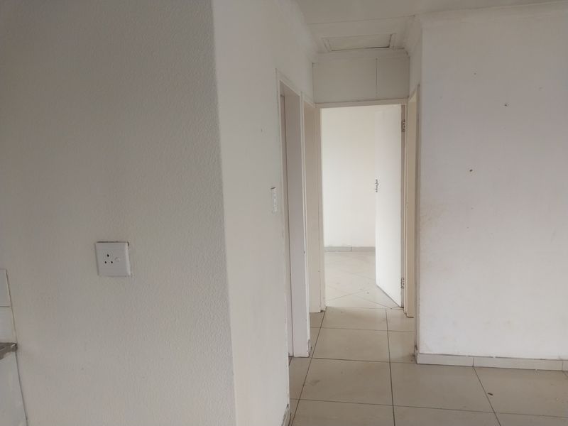 A vacant hallway featuring tiled flooring and neutral walls, providing access to adjacent rooms within the property.