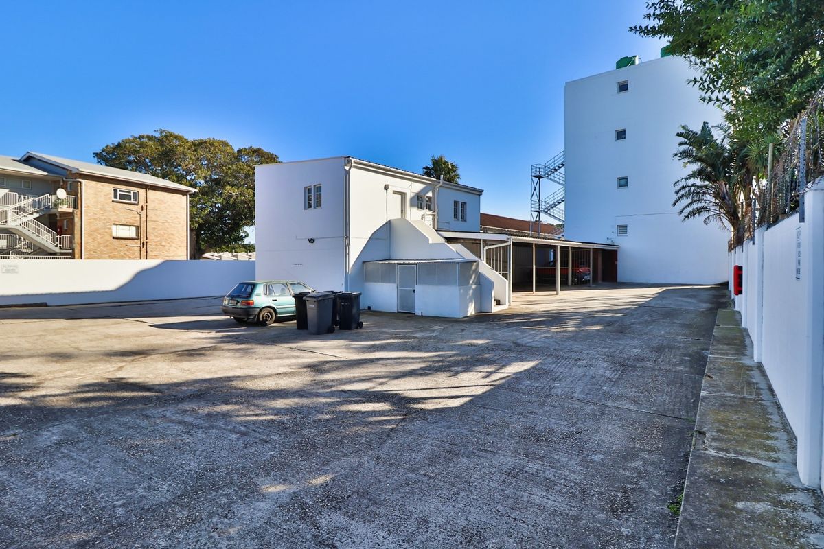 Rear exterior view of the apartment complex featuring a large concrete parking area, covered parking bays, and perimeter boundary walls.
