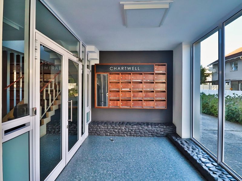 A bright and modern apartment building entrance lobby featuring built-in wooden mailboxes, large glass windows, and durable terrazzo flooring.