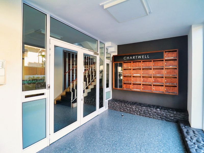Modern apartment building entrance lobby featuring glass doors, a wall-mounted mailbox unit, stone feature wall, and durable terrazzo flooring.