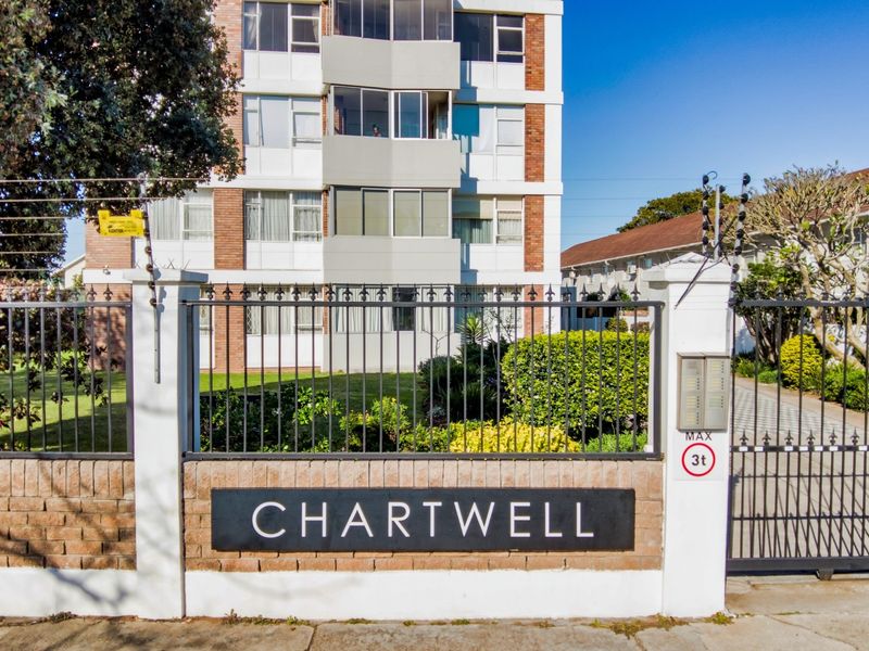 Front entrance view of Chartwell apartment complex featuring a secure gated access point, brick boundary wall, and electric fencing.