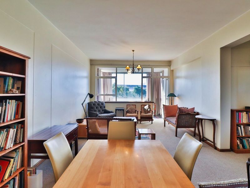 Spacious open-plan living and dining area featuring large windows that provide natural light and views, with neutral wall finishes and carpeted flooring.