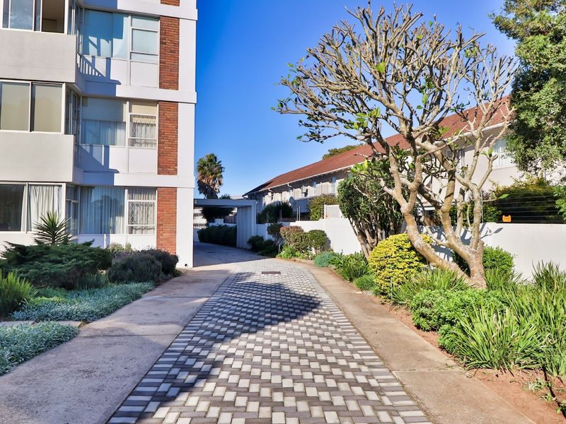 A well-maintained exterior view of the apartment complex featuring a paved driveway, landscaped garden areas, and a clean brick and concrete facade.
